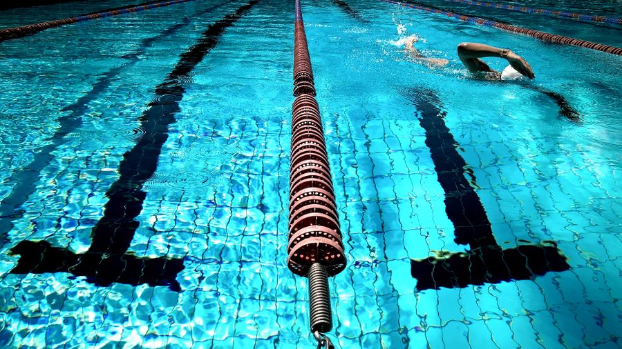 Swimmer in a white cap doing freestyle in a bright turquoise lap pool with red lane ropes